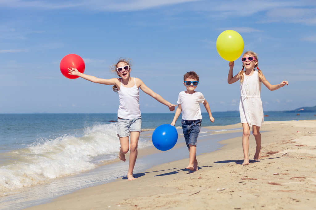Three happy children with balloons playing on the beach at the day time. Concept of happy friendly family.