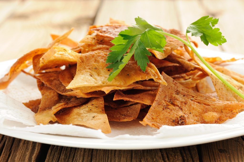 Fried triangle lavash chips in white plate with fresh parsley