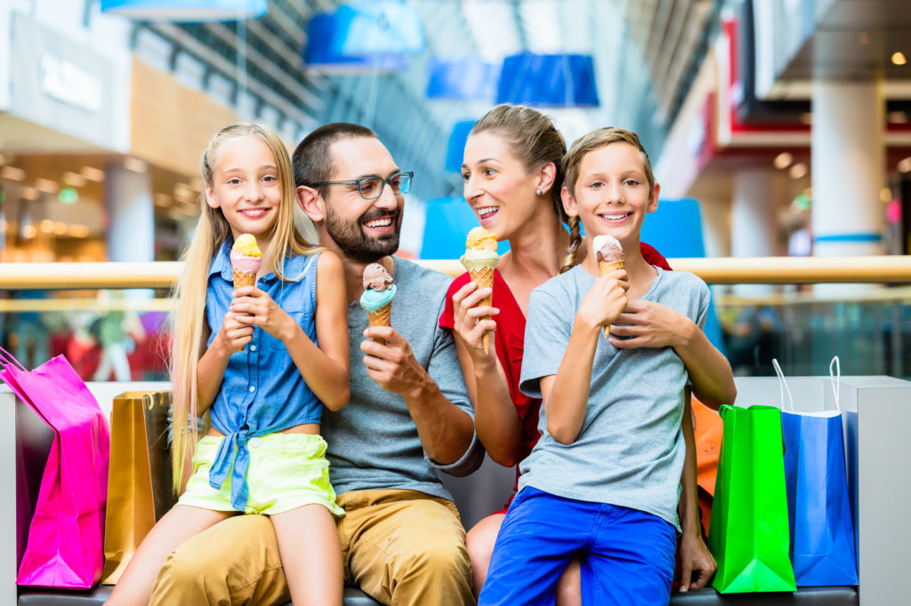 Family eating ice cream in shopping mall with bags