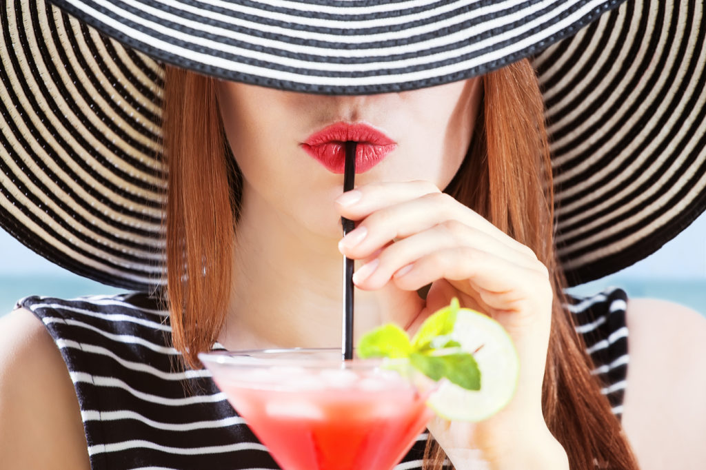 young woman in sunhat drinks cocktial