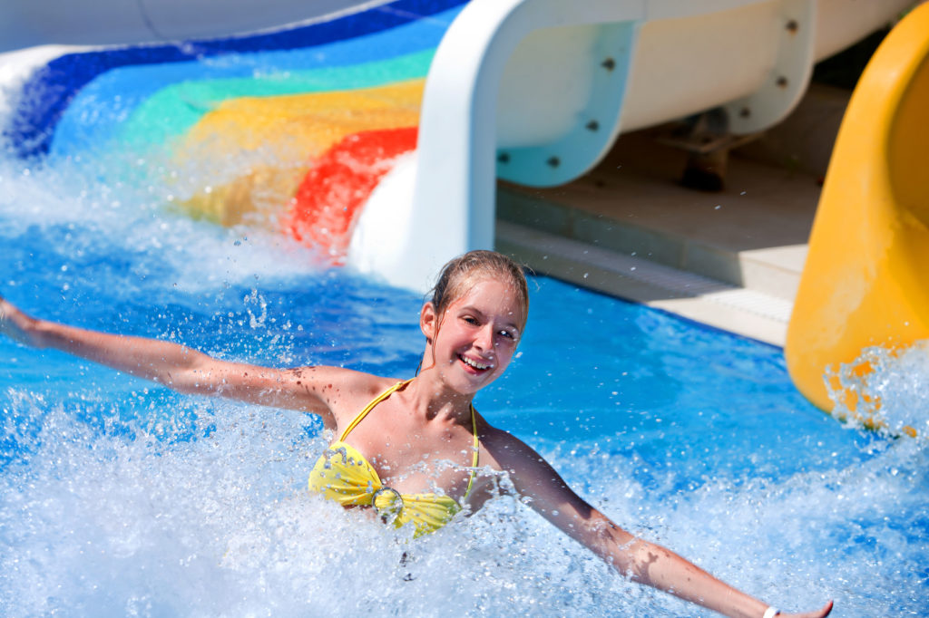 Happt teen girl on water slide at aquapark. Summer holiday.