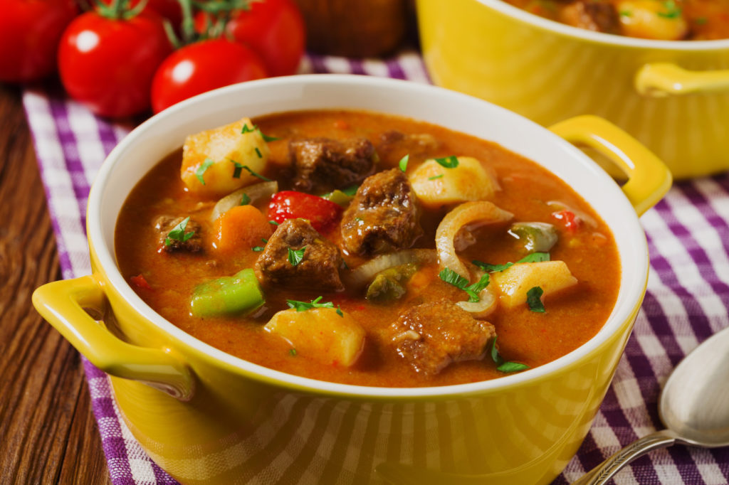Beef stew served with cooked potatoes in a yellow little pot on a wooden background.