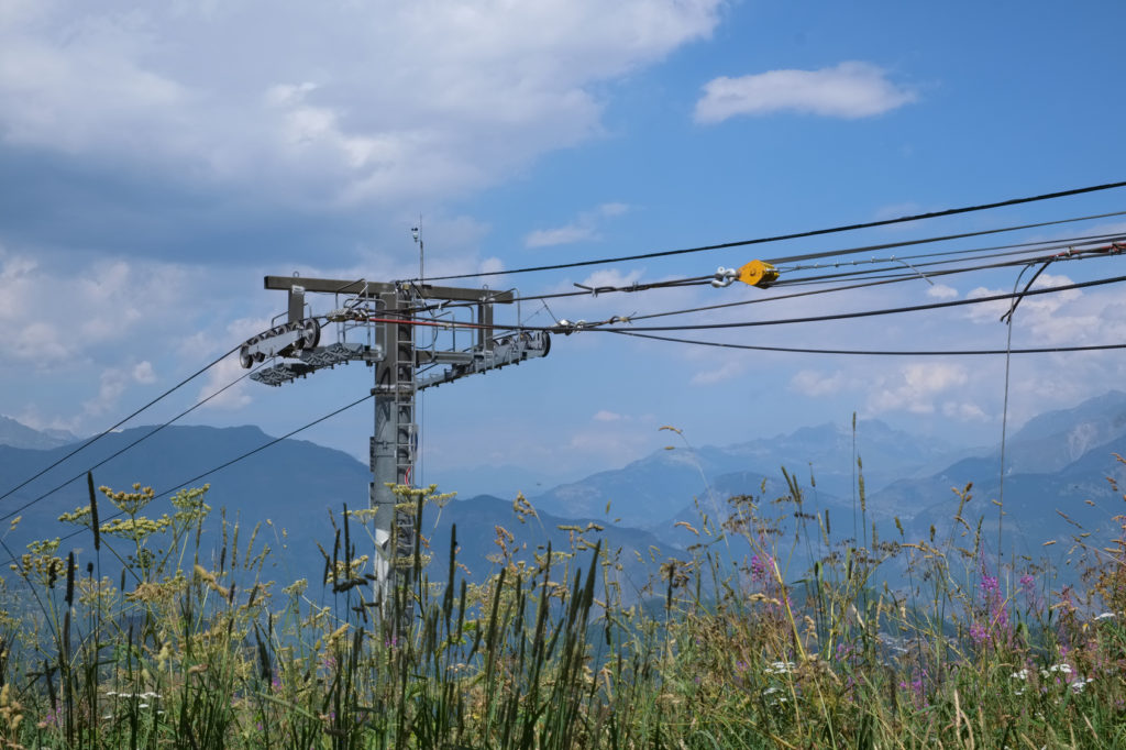 Ski lift tower with a lot of steel wires hanging in front of a rocky mountain summer landscape