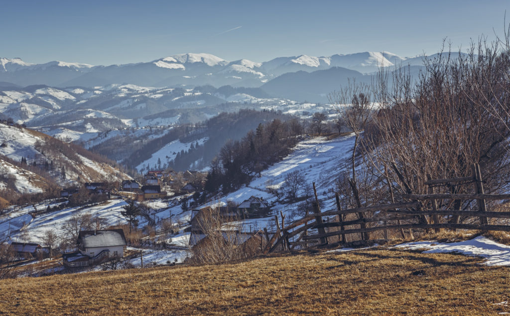 Rural scenery with traditional Romanian hamlet during first snow on a sunny winter morning in Magura village, Brasov county, Transylvania region, Romania.