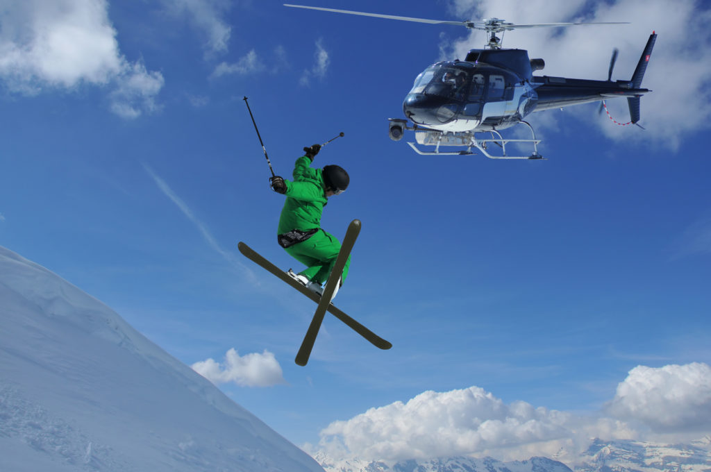 helicopter equiped with a steady cam filming a ski jumper in green clothes crossing his skis for a high jump