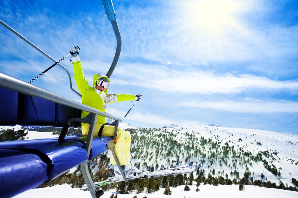 Happy young woman skier sit on ski lift chair, smiling and cheerfully lifting her hands