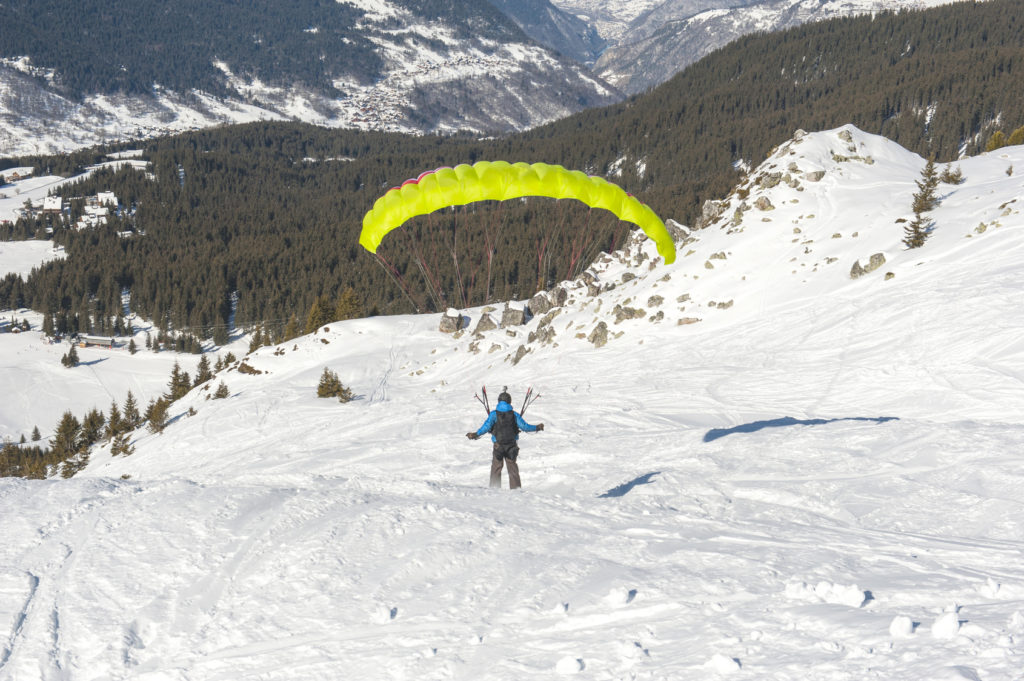 Paraglider taking off from a snow covered slope looking down an alpine mountain valley