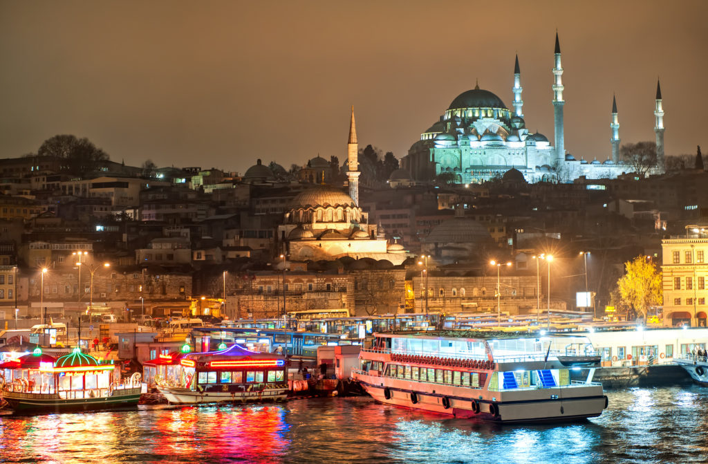 Istanbul skyline from Galata bridge over Golden Horn by night, with Suleymaniye mosque and fish boat restaurants in Eminonu